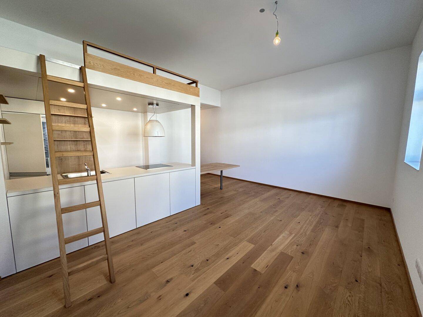Detailansicht der kompakten Küchenzeile mit integriertem Hochbett und Holzleiter in einem hellen Raum.