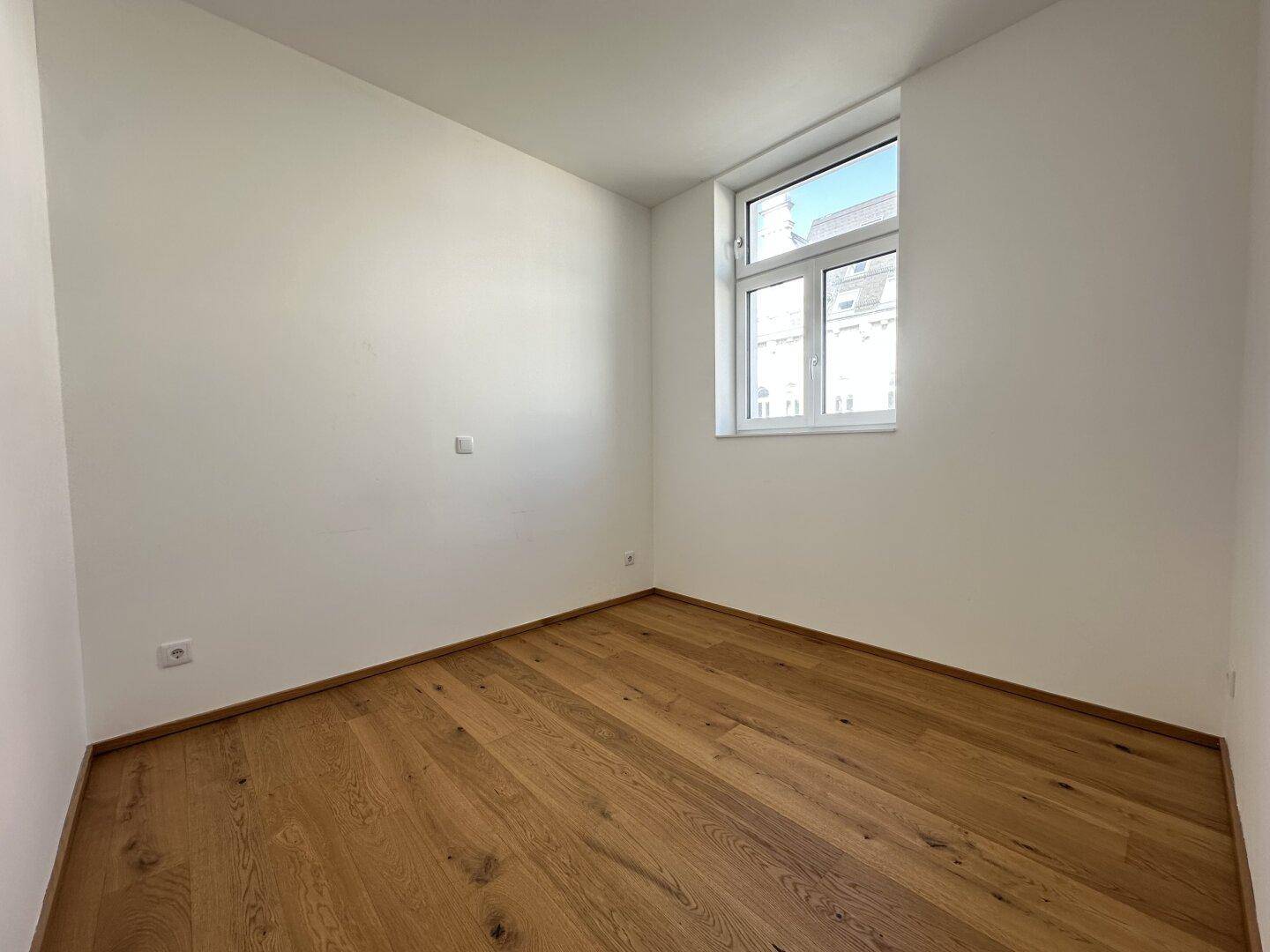 Ruhiges Zimmer mit Parkettboden und einem Fenster, ideal als Schlaf- oder Arbeitszimmer nutzbar.
