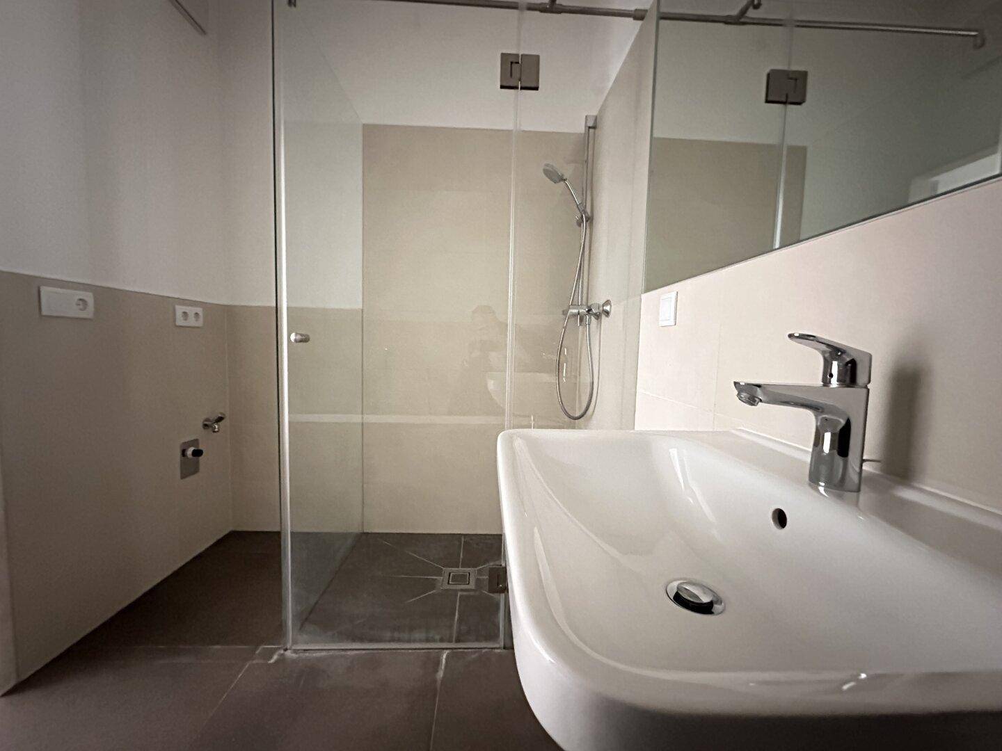 Modernes Badezimmer mit ebenerdiger Dusche, eleganten Fliesen und einem einzelnen Waschbecken.