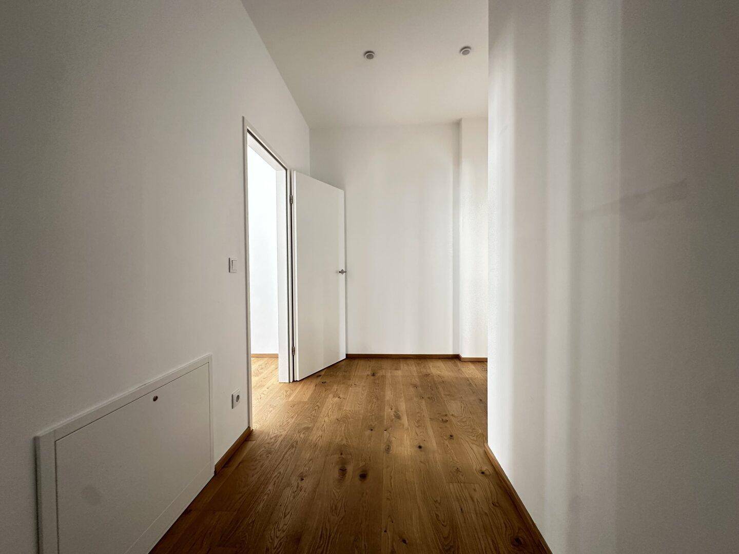 Heller Flur mit Holzparkettboden und weiß gestrichenen Wänden, der zu weiteren Räumen führt.