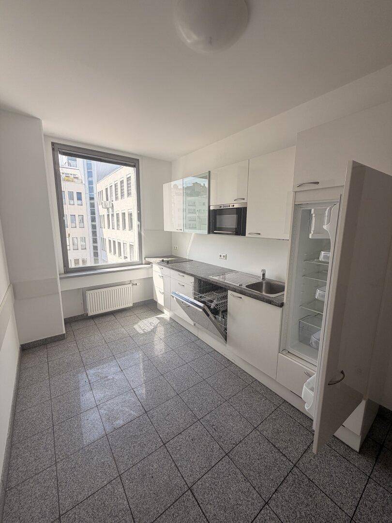 Moderne Einbauküche mit weißen Hochglanzschränken, Spülmaschine und Kühlschrank, bietet viel Stauraum.
