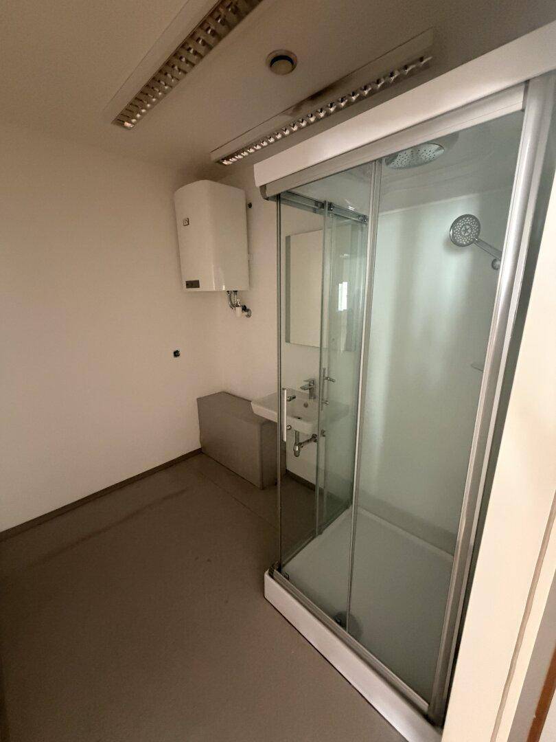 Kleines Badezimmer mit Duschkabine, Waschbecken und Warmwasserboiler, funktional und hell.