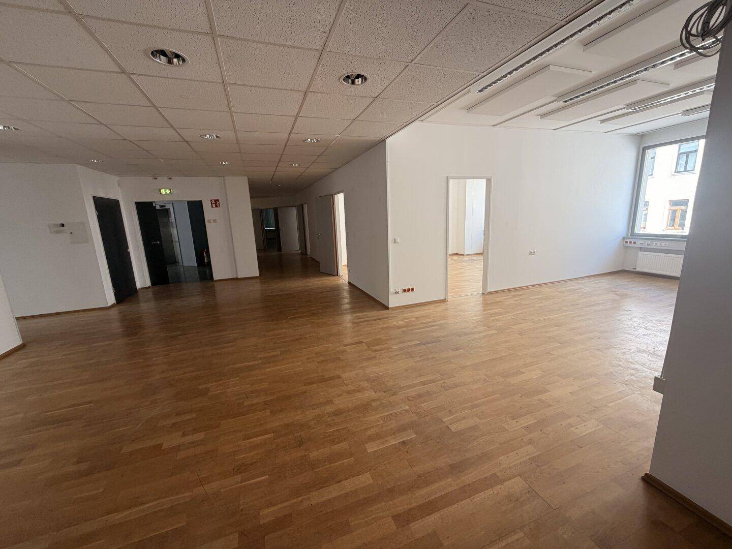 Weitläufiger Bürobereich mit Holzparkett und weiß gestrichenen Wänden, bietet viel Platz für Arbeitsplätze.