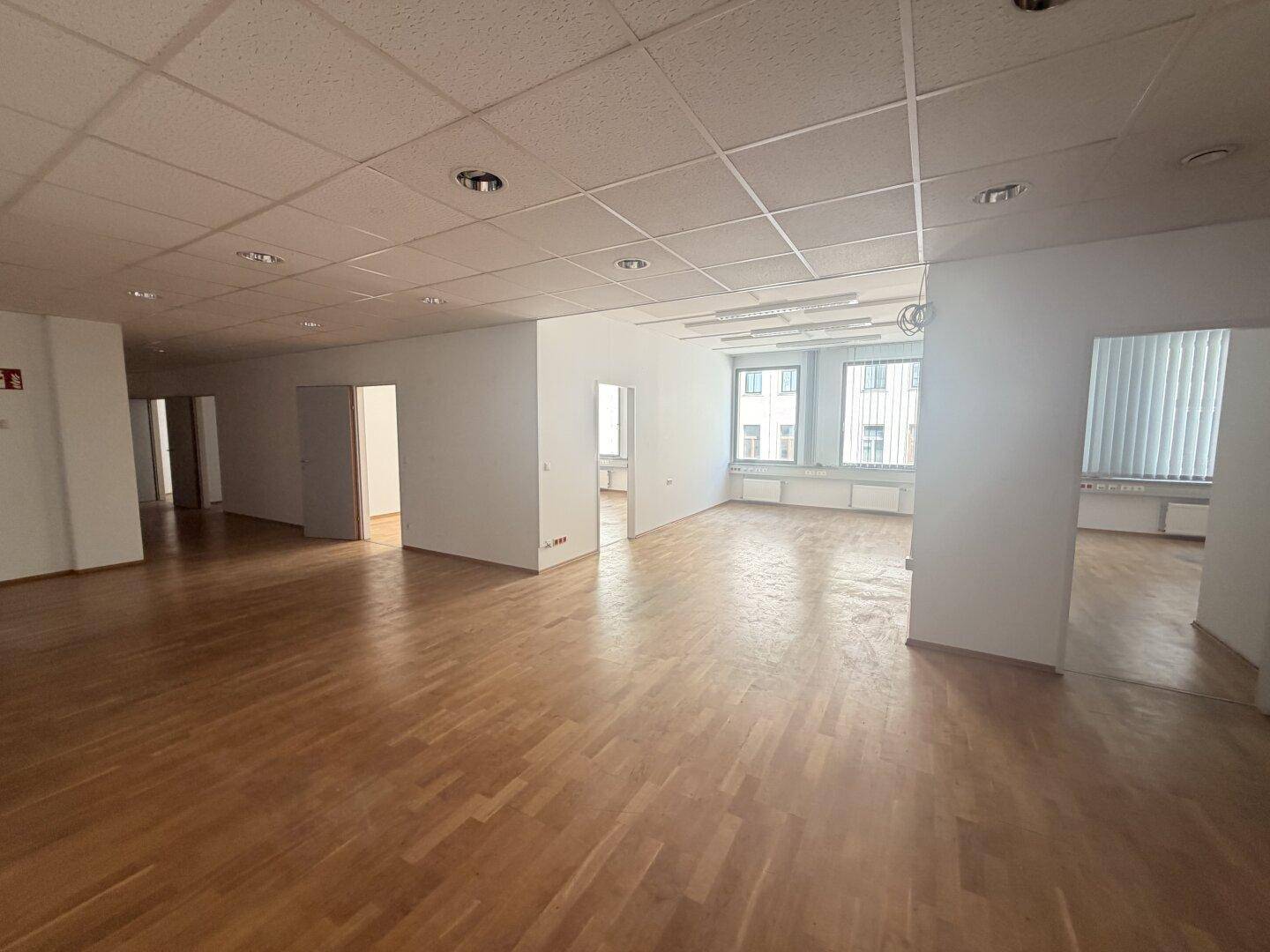 Heller, offener Büroraum mit Holzparkett und großen Fenstern, die viel Tageslicht hereinlassen.
