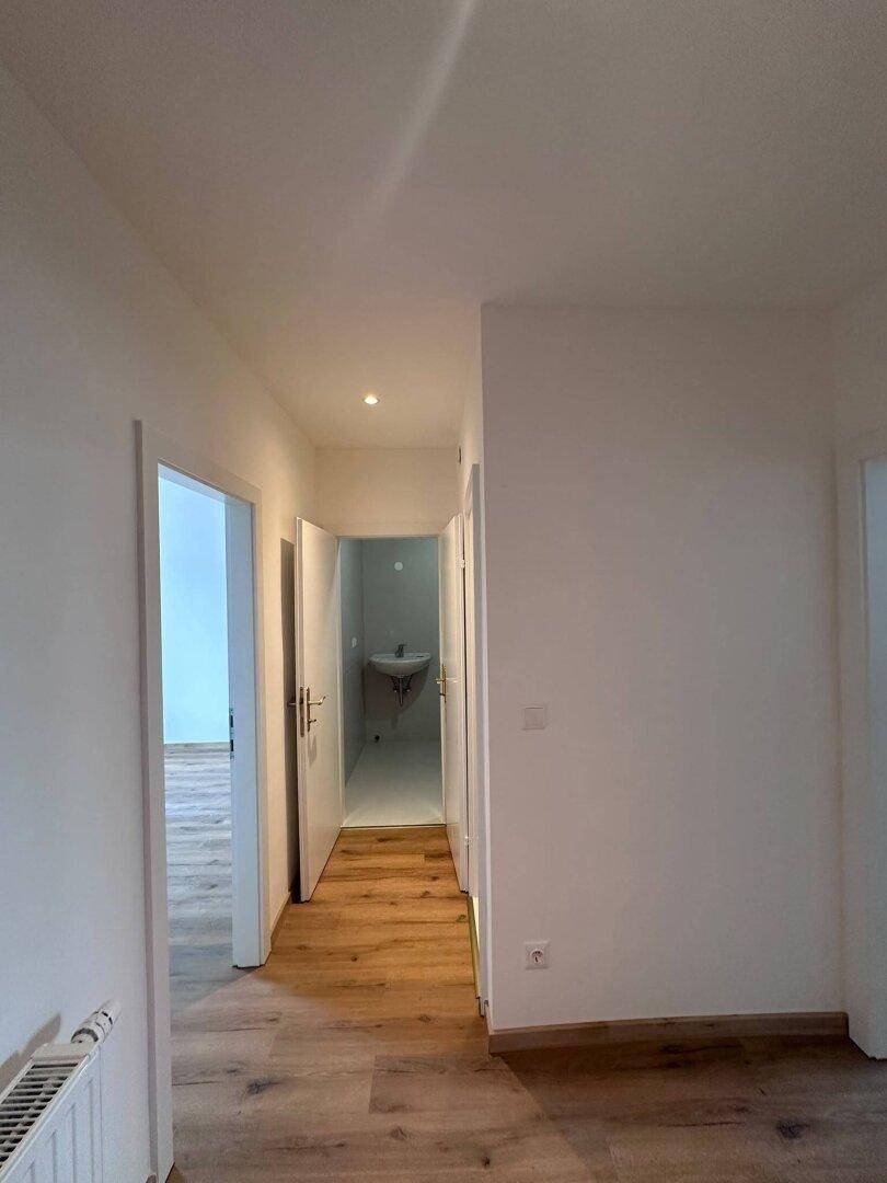 Heller Flur mit Laminatboden und Zugang zu einem Badezimmer mit Waschbecken.