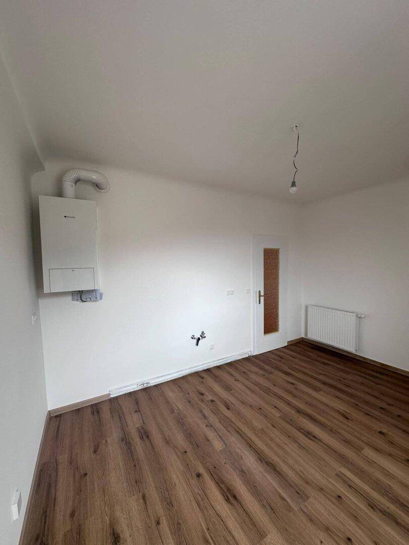 Leerer Raum mit Laminatboden, Heizungsanlage an der Wand und einem Heizkörper.