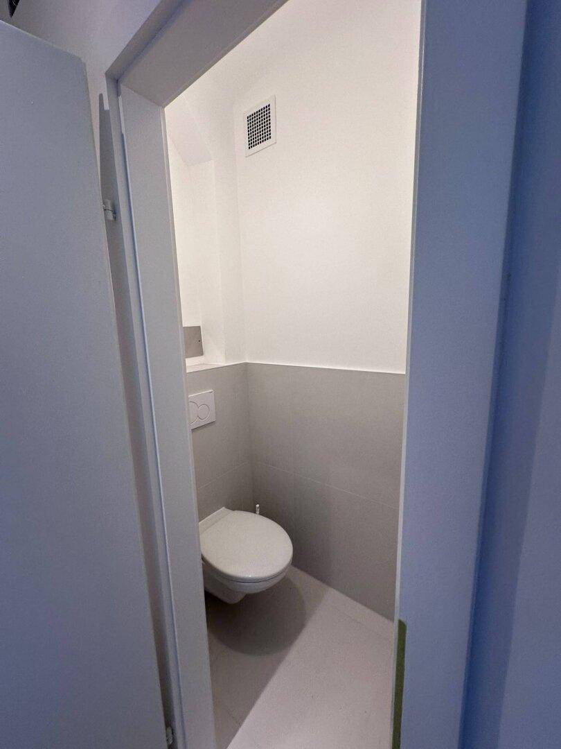 Modernes Gäste-WC mit Wand-WC und grauen Fliesen im unteren Bereich.