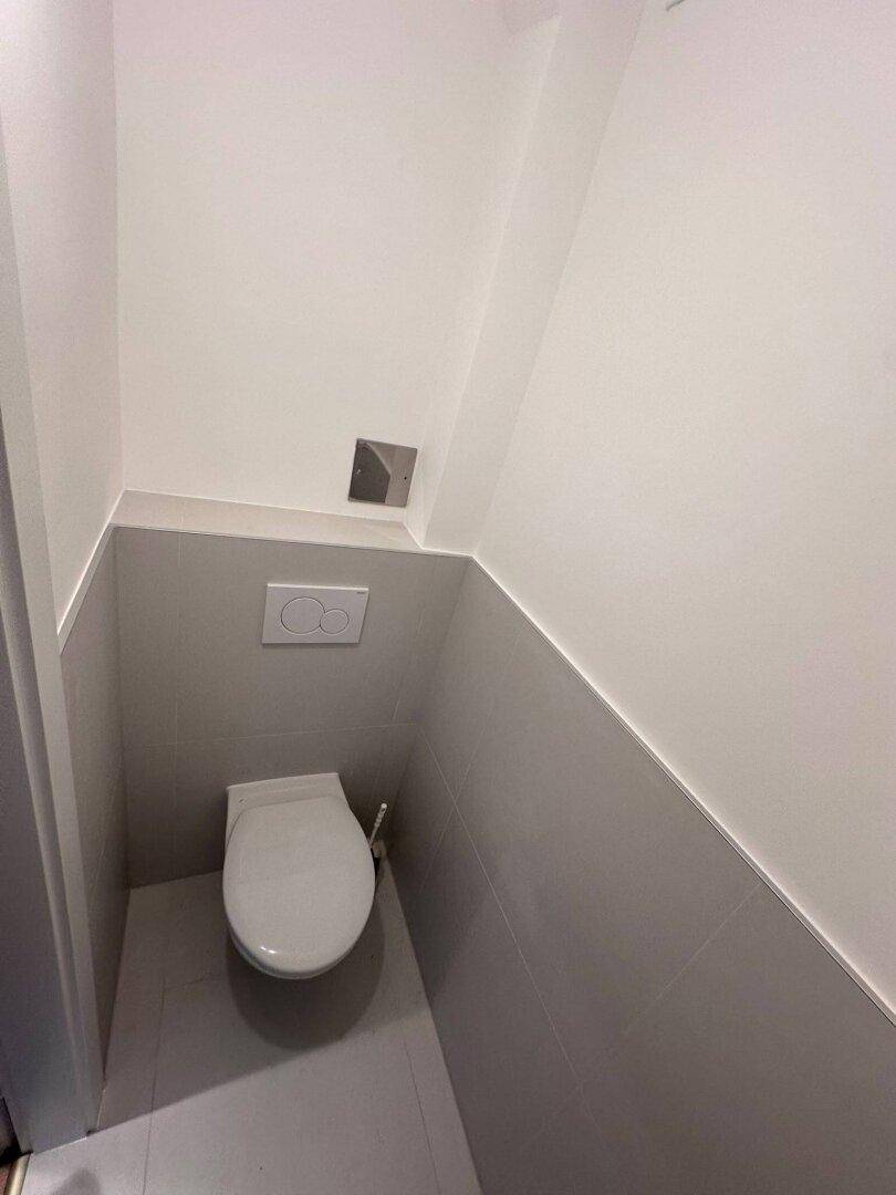 Kleines, funktionales Gäste-WC mit Wand-WC und grauen Fliesen an den Wänden.