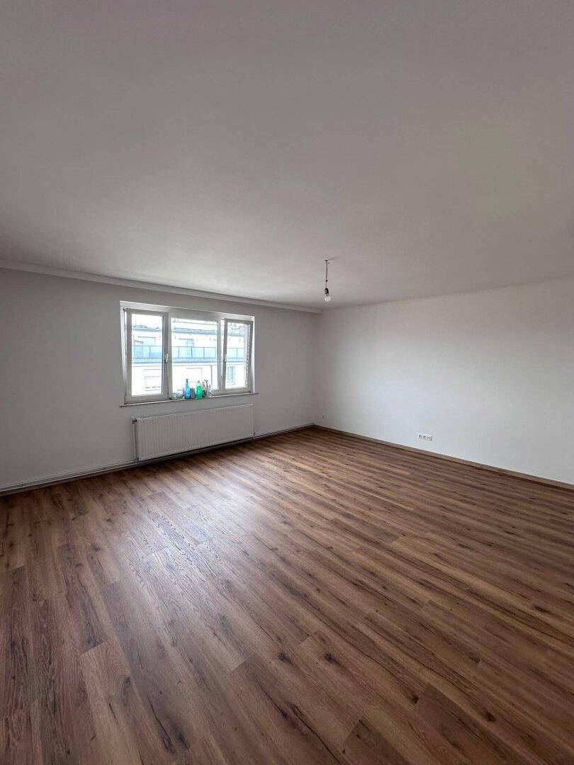 Geräumiges Wohnzimmer mit Laminatboden und einem großen Fenster, das viel Licht spendet.