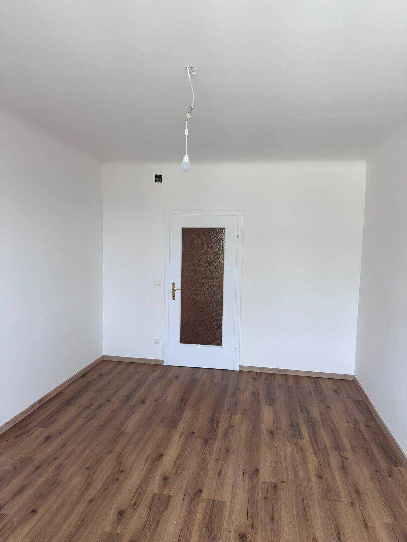 Leeres Schlafzimmer mit Laminatboden und einer Tür mit Milchglaseinsatz.