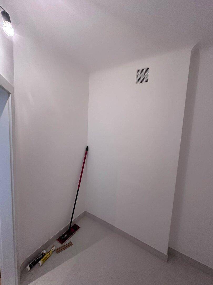 Kleiner Abstellraum mit Reinigungsutensilien und Lüftungsgitter an der Decke.