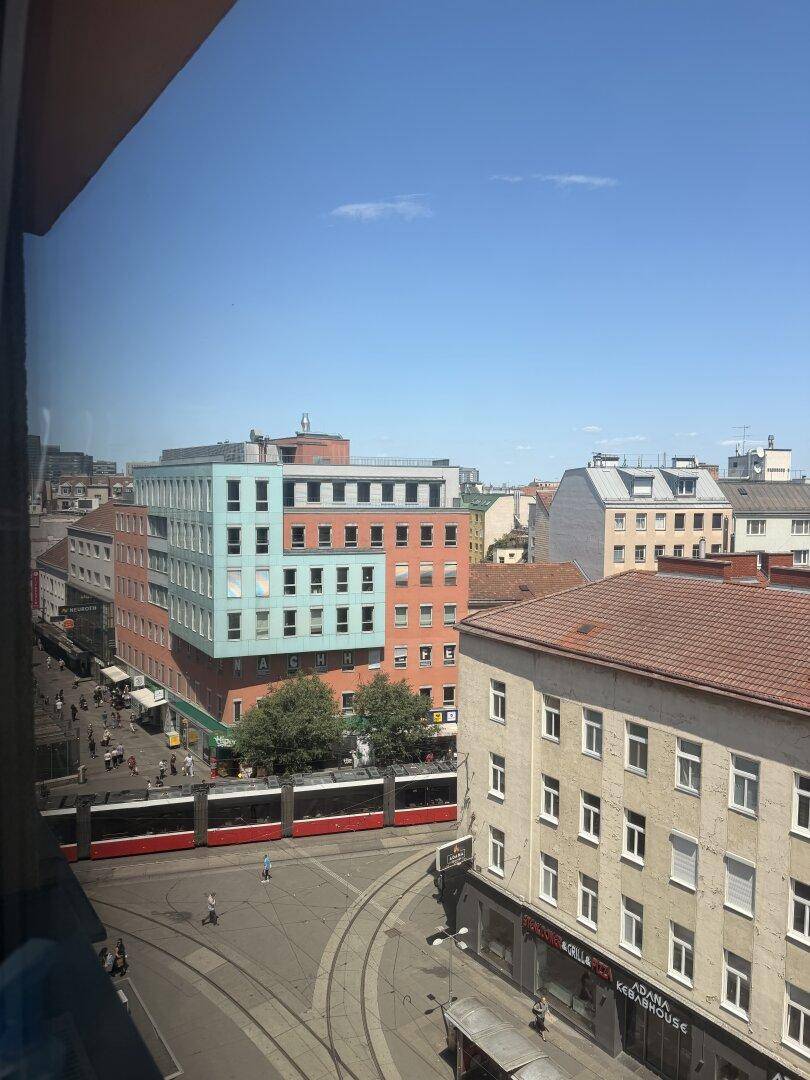 Blick aus dem Fenster auf eine belebte Stadtstraße mit Straßenbahn und Gebäuden.