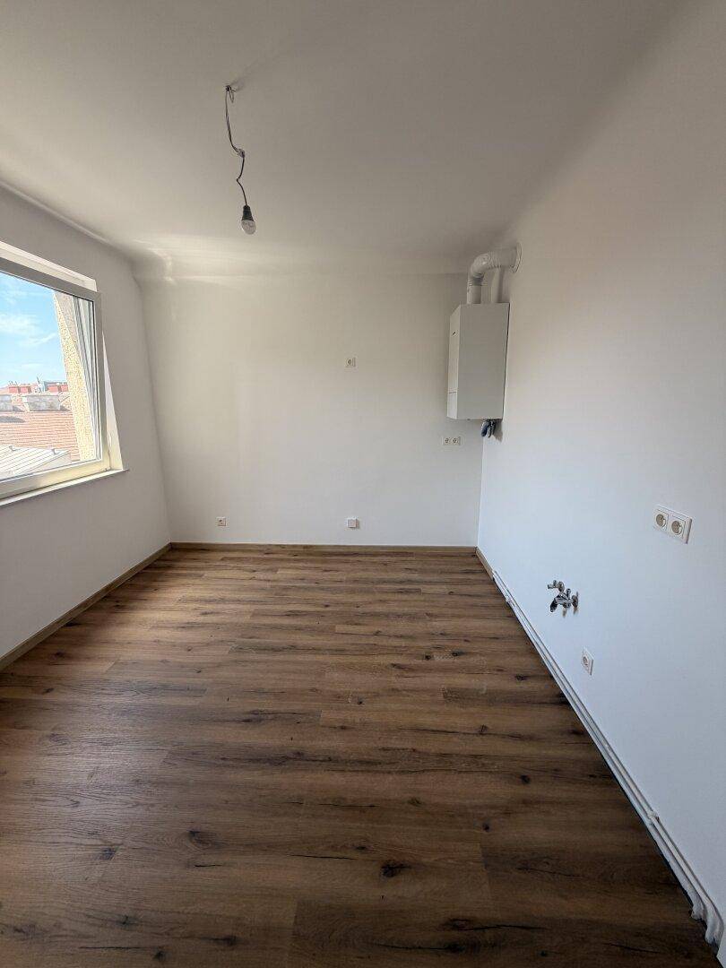 Leerer Raum mit Laminatboden, Fenster und einer Heizungsanlage an der Wand.