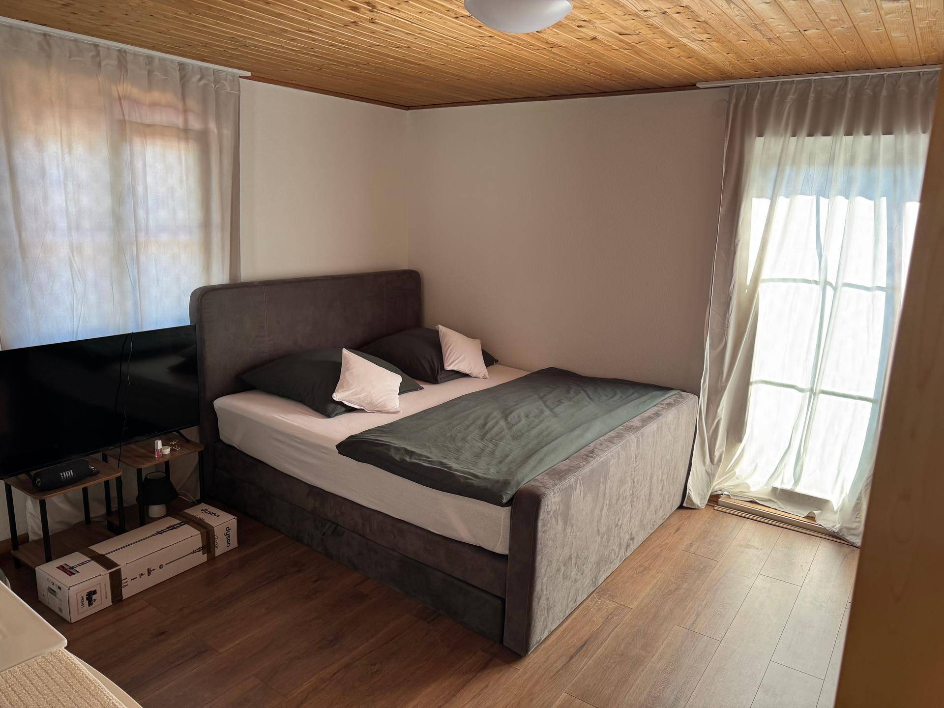 Helles Schlafzimmer mit Holzboden und -decke, einem komfortablen Bett und Zugang zu einem Außenbereich.