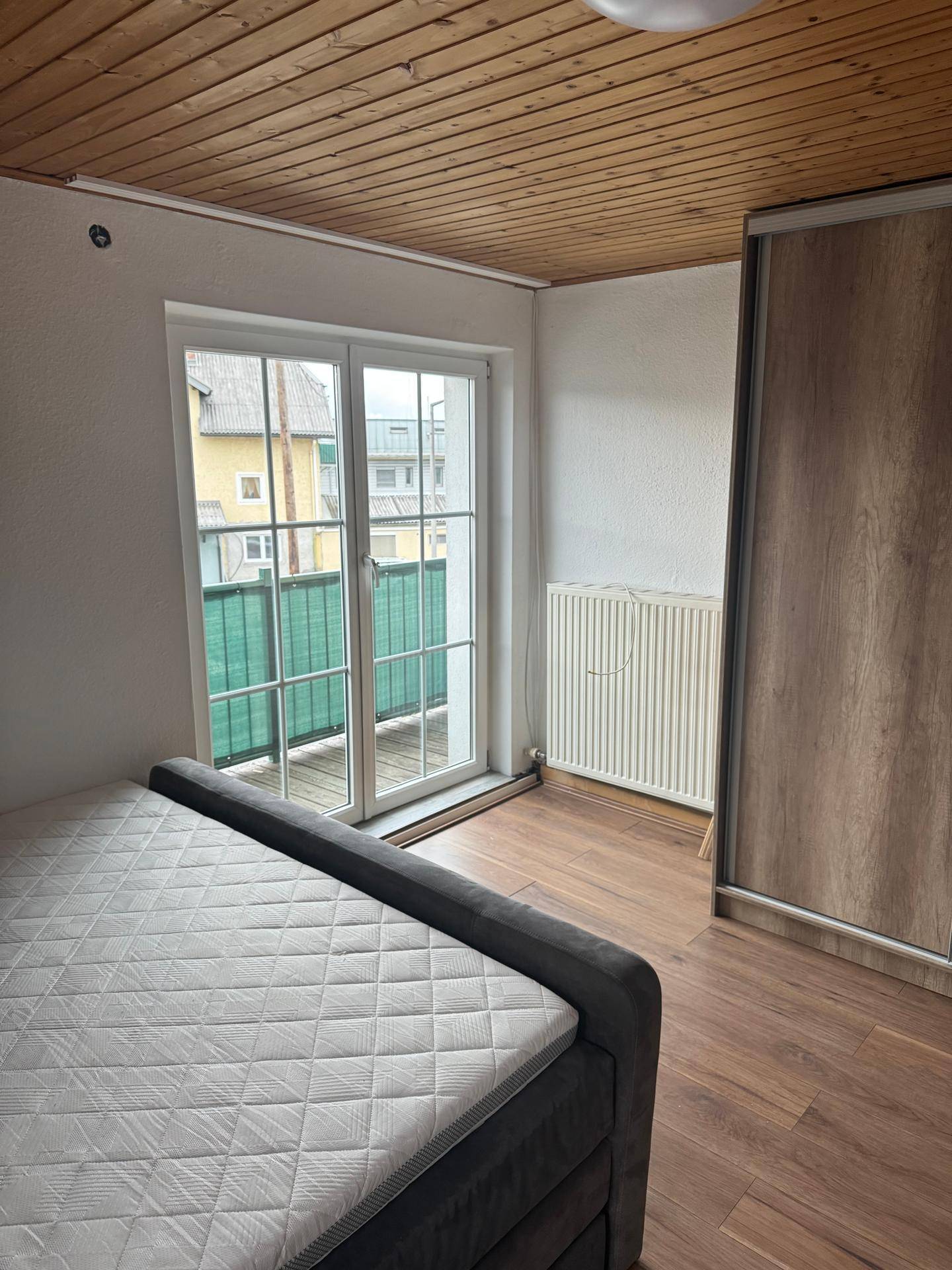 Schlafzimmer mit Holzboden, Holzdecke, Einbauschrank und Zugang zu einem Balkon.
