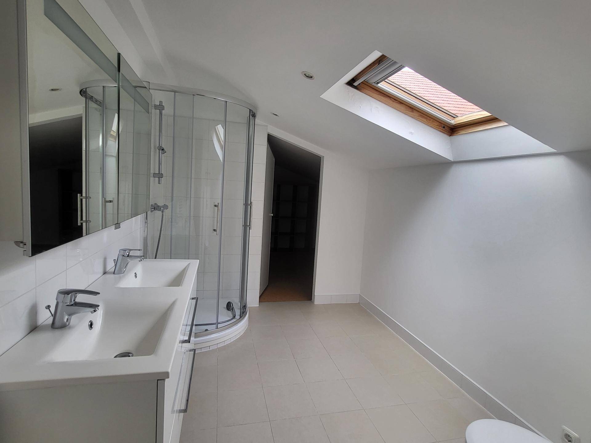 Modernes Badezimmer mit zwei Waschbecken, Duschkabine und Dachfenster, das viel Licht spendet.