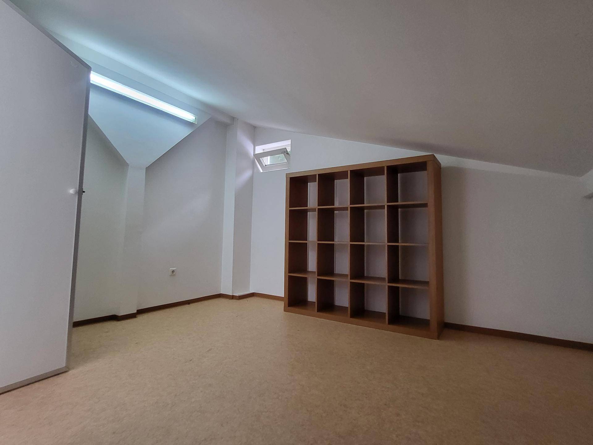 Schlafzimmer mit Dachschräge, Regal und Laminatboden, beleuchtet durch ein Oberlicht.