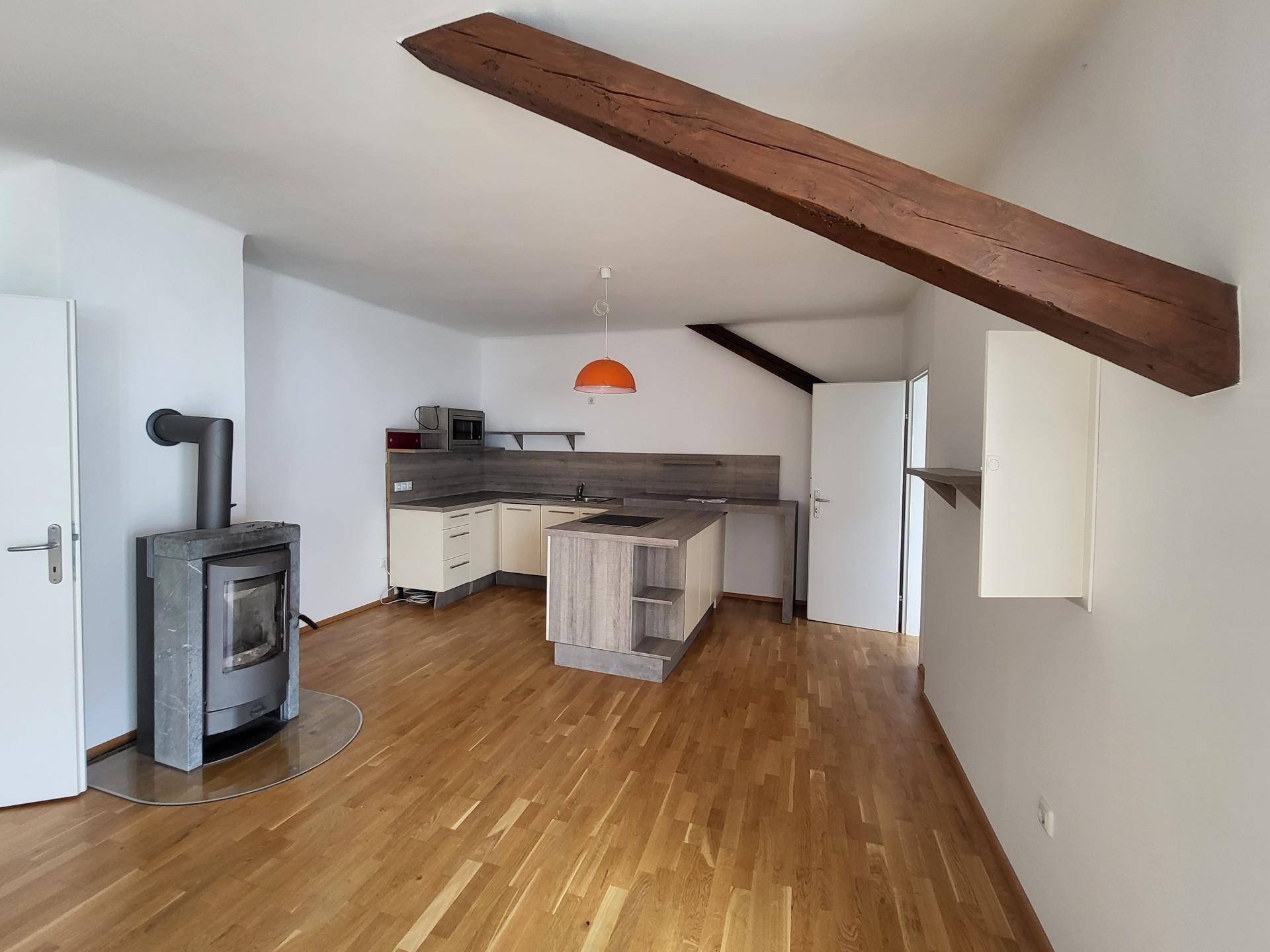 Offene Küche mit Kücheninsel und Kaminofen in einem hellen Wohnbereich mit Holzbalken.