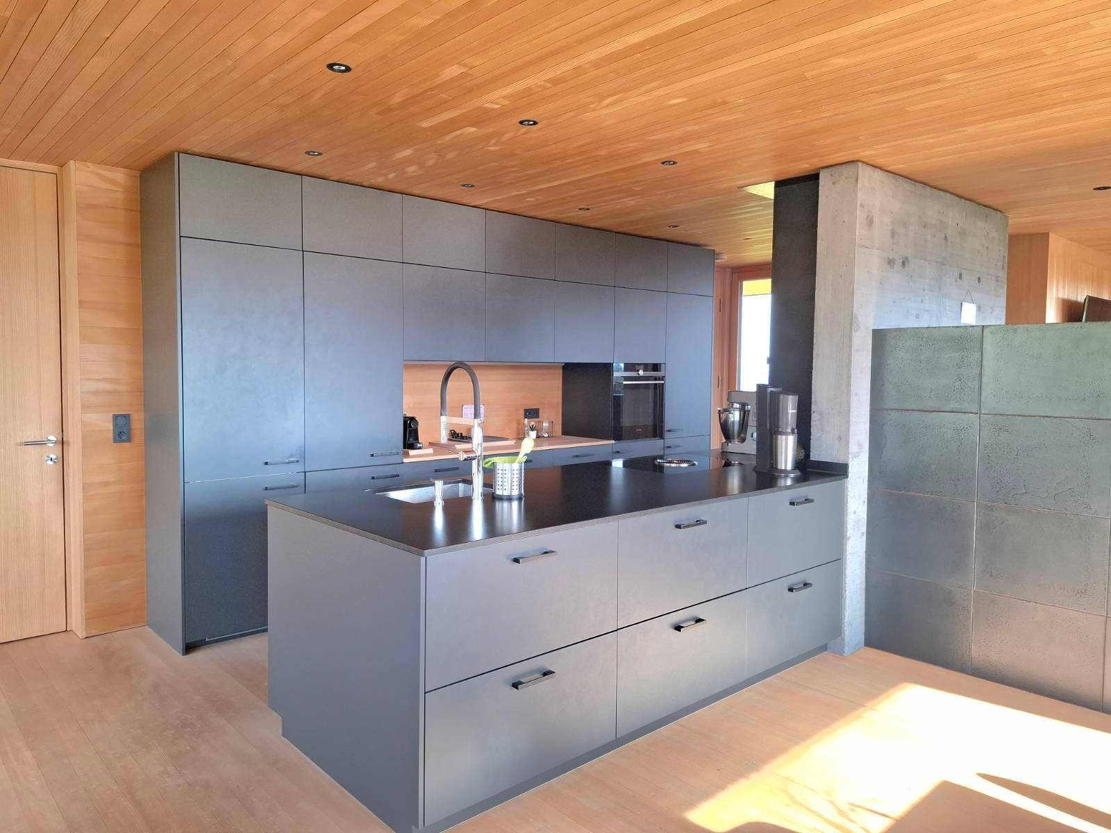 Geräumige, moderne Küche mit Kücheninsel, dunklen Fronten und Holzboden in hellem Ambiente.