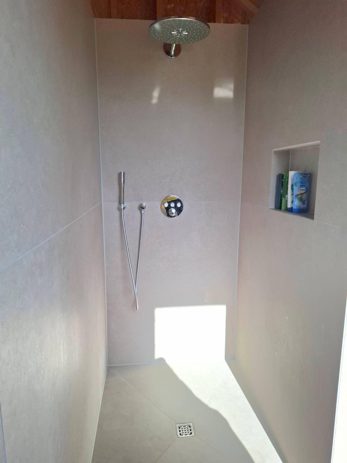 Moderne Dusche mit Regenduschkopf und hellen Fliesen in einem lichtdurchfluteten Badezimmer.