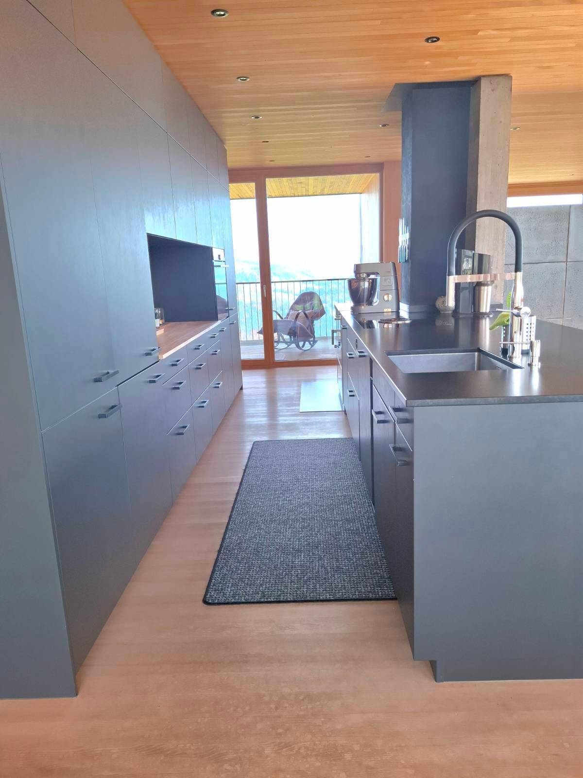 Moderne Küche mit dunklen Schränken, Holzboden und Zugang zu einer Terrasse mit Bergblick.