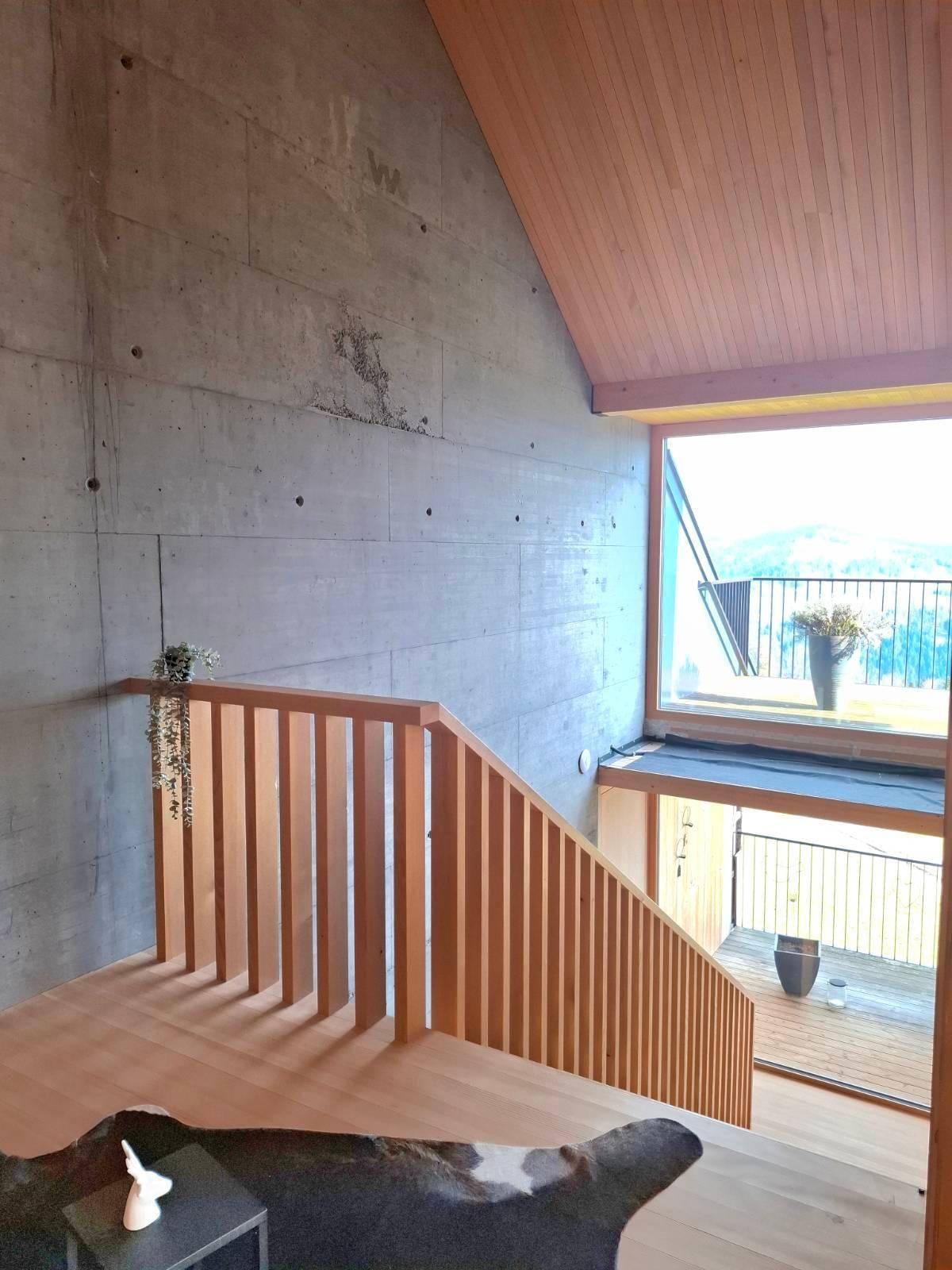 Treppenhaus mit Holzboden und Geländer, Sichtbetonwand und Blick auf die Landschaft.