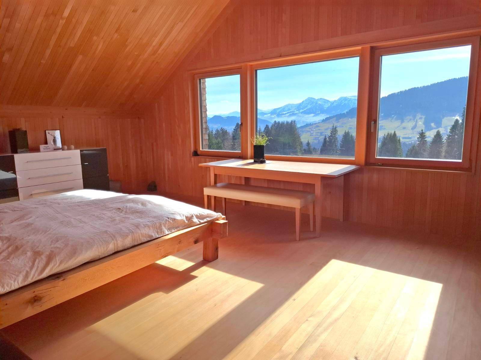 Helles Schlafzimmer mit Holzbett, Holzwänden und Panoramablick auf die umliegende Natur.