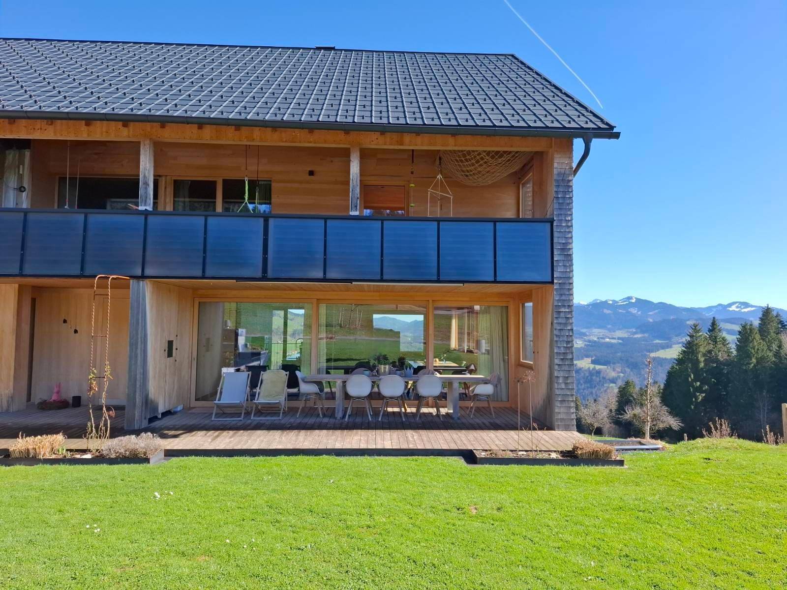 Fassade des Holzhauses mit großen Glasfronten, Terrasse und Balkon mit Blick auf die Landschaft.