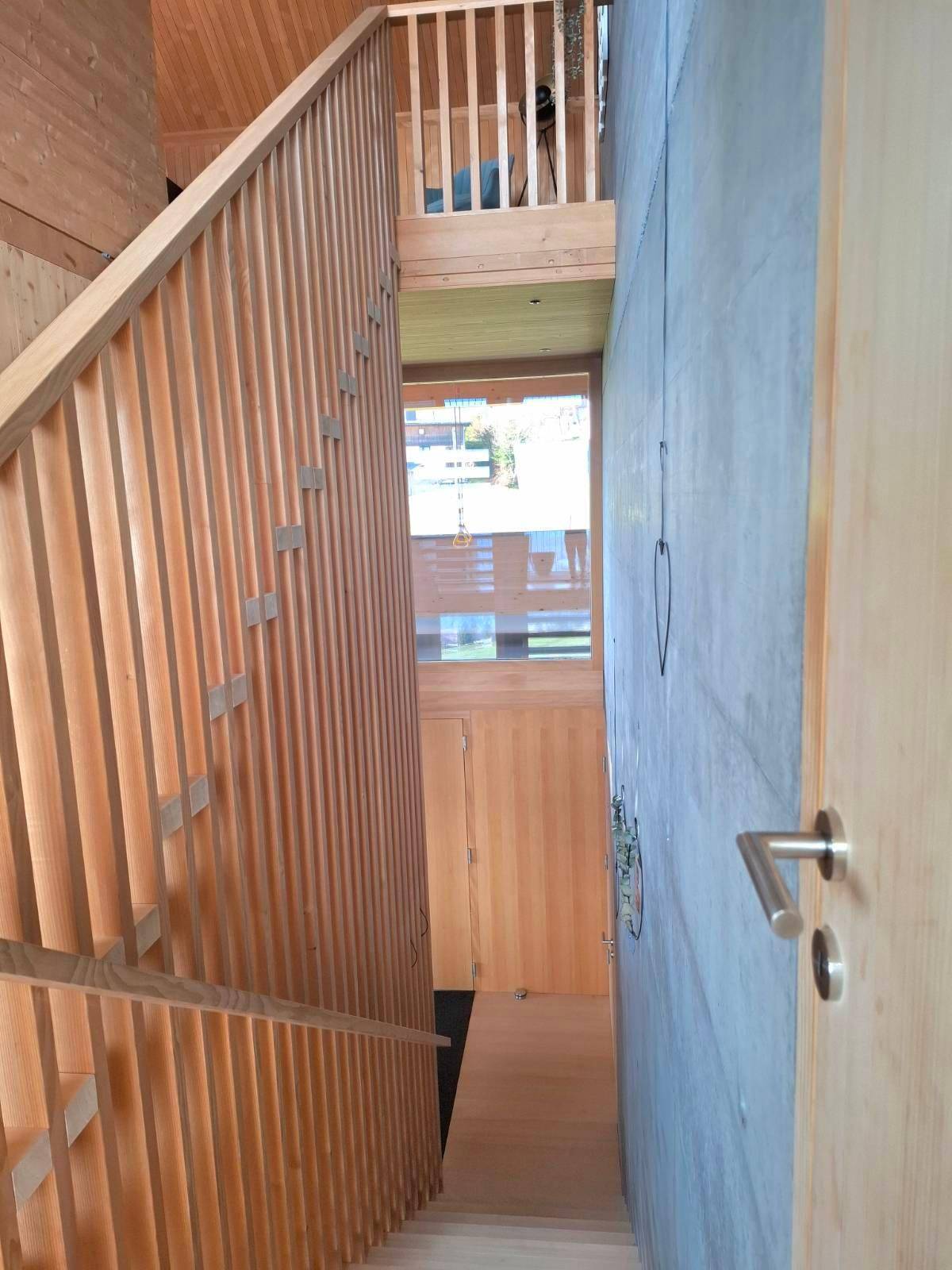 Heller Treppenaufgang mit Holzgeländer und Sichtbetonwand, der verschiedene Ebenen verbindet.