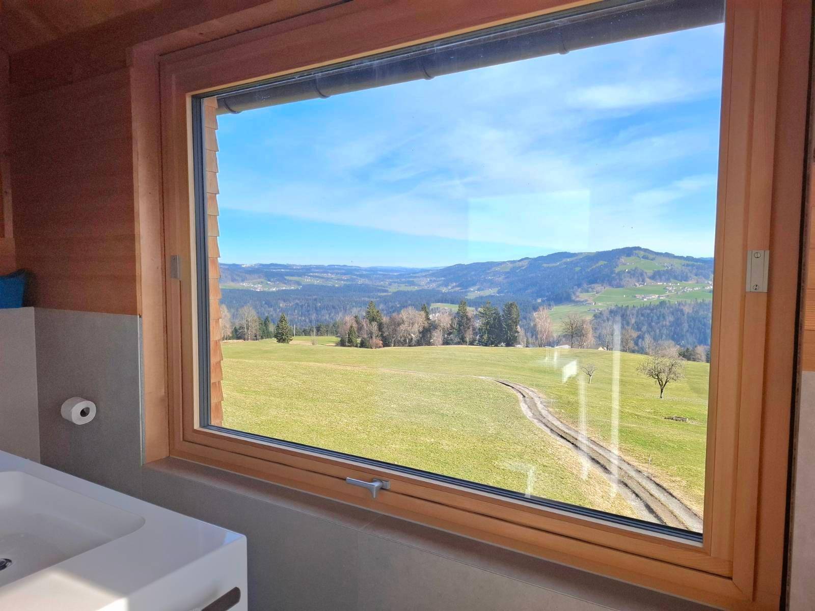 Badezimmer mit großem Fenster, das einen weiten Blick auf die grüne Landschaft bietet.