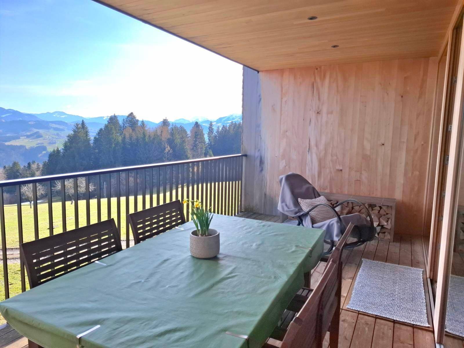Überdachter Balkon mit Esstisch und Holzstapel, bietet einen weiten Blick auf die Berge.