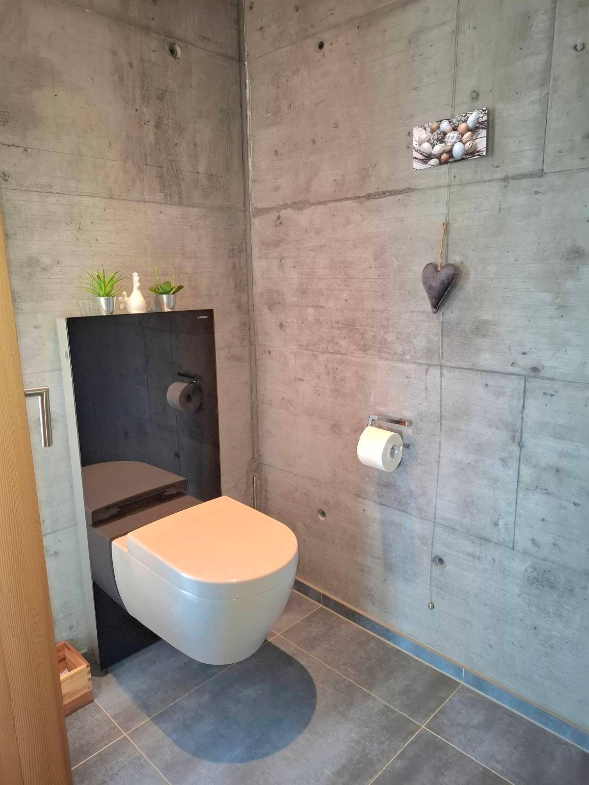 Modernes WC mit Wand-WC und Sichtbetonwänden, minimalistisch gestaltet.