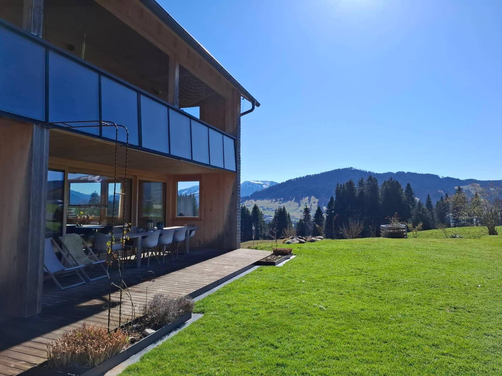 Großer Rasenbereich neben dem Haus mit weitem Blick auf die umliegende Berglandschaft und Wälder.