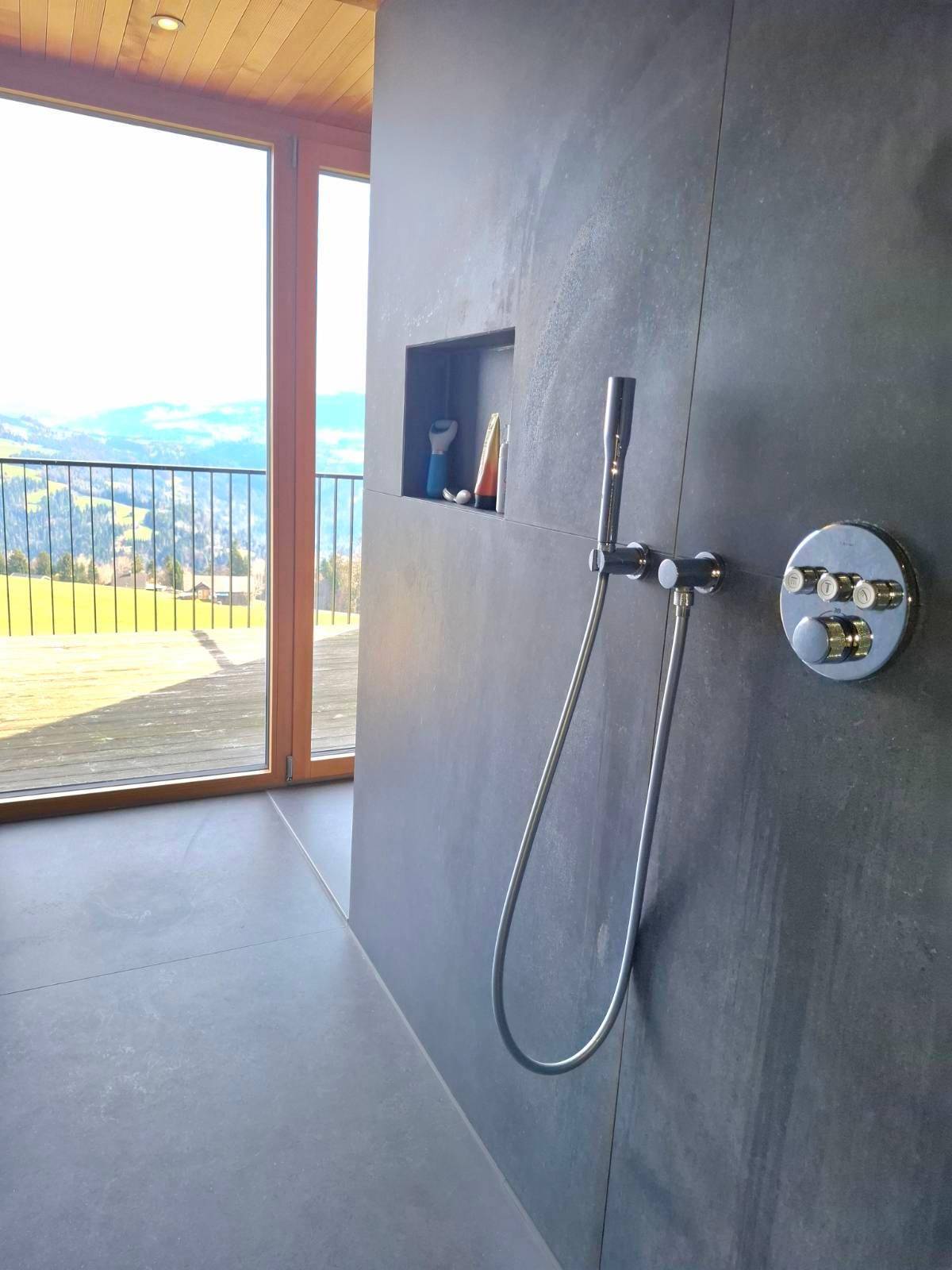 Moderne Dusche mit dunklen Fliesen und integrierter Nische, bietet einen Blick ins Grüne.