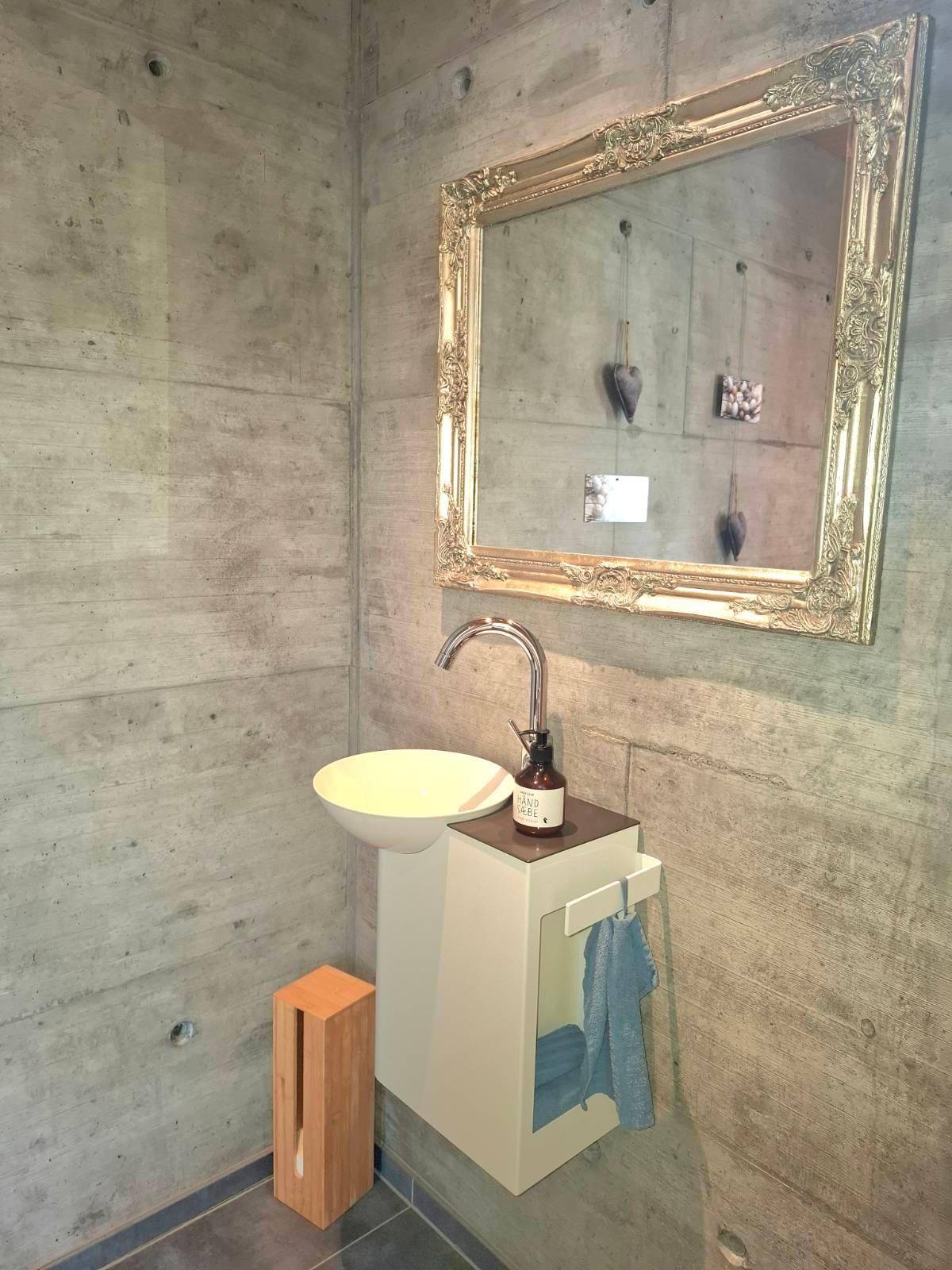 Modernes Gäste-WC mit Waschbecken, Spiegel und Sichtbetonwänden.
