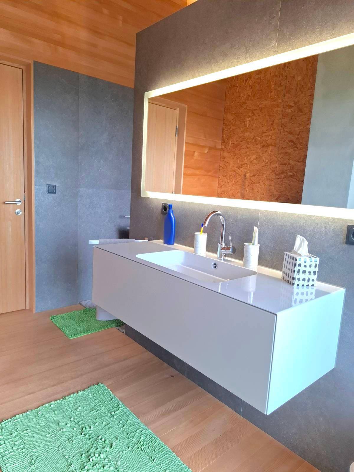 Modernes Badezimmer mit Einzelwaschbecken, beleuchtetem Spiegel und Holzboden.