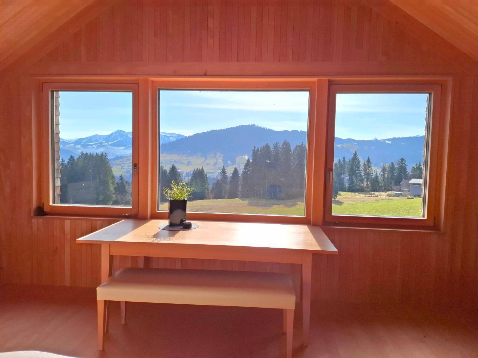 Schlafzimmer mit Holzwänden, Holzboden und großen Fenstern mit weitem Blick auf die Berge.