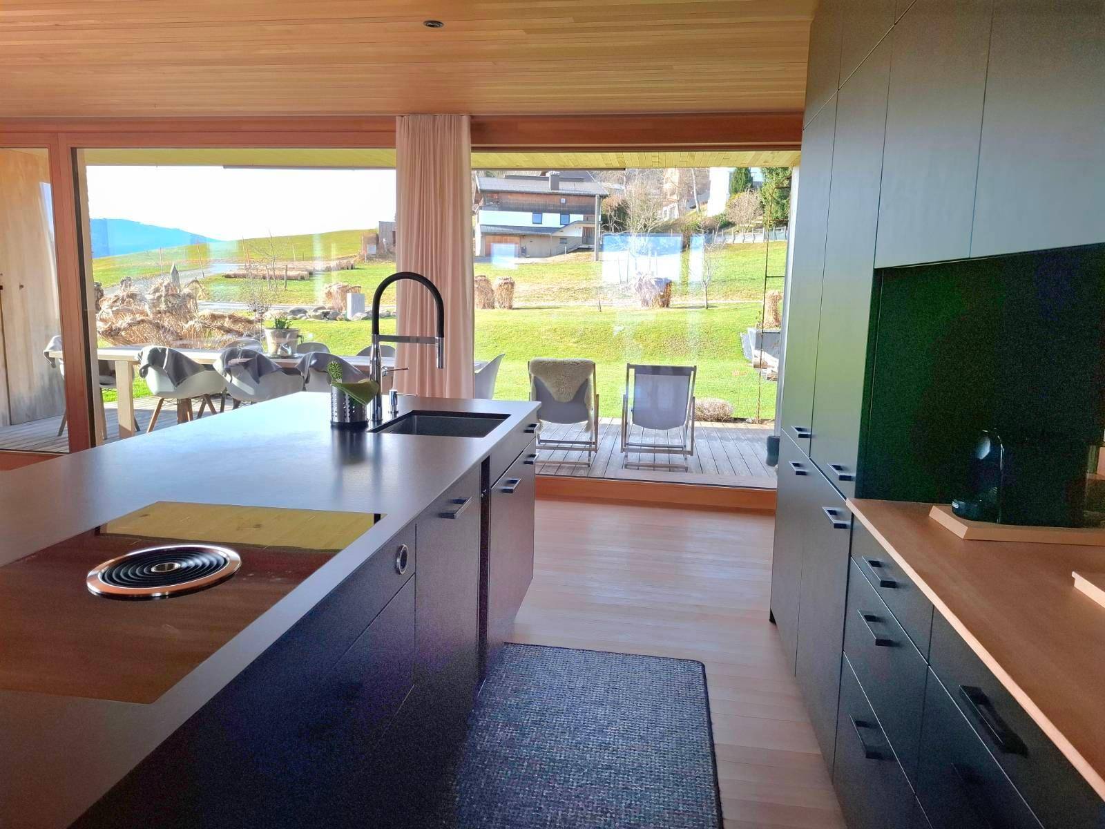 Helle Küche mit Kücheninsel, dunklen Fronten und großen Fenstern mit Blick auf den Garten.