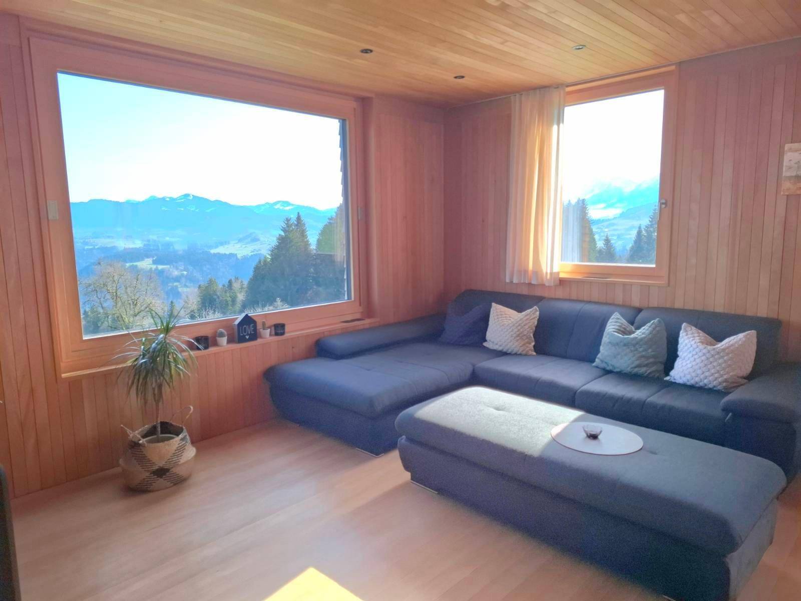 Helles Wohnzimmer mit Holzwänden, großem Sofa und Panoramablick auf die Berglandschaft.