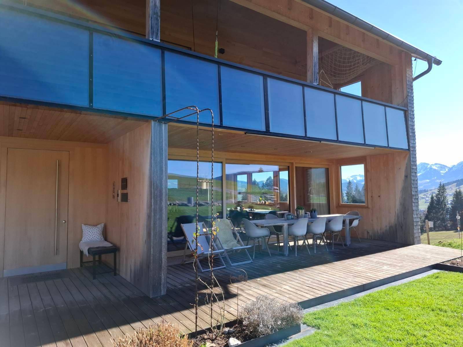 Detailansicht der Holzfassade mit Terrasse und Balkon, umgeben von grüner Natur und Bergblick.