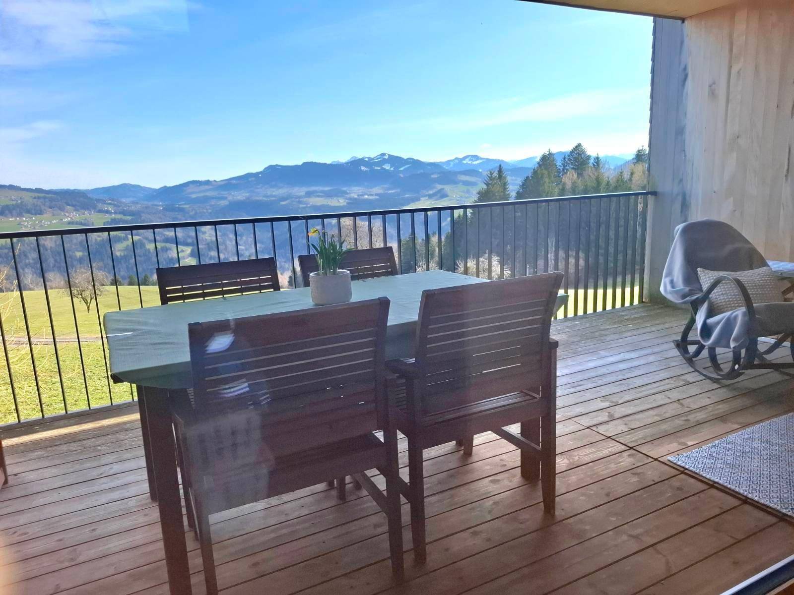 Balkon mit Esstisch und Stühlen, bietet einen weiten Blick auf die Berge und grüne Landschaft.