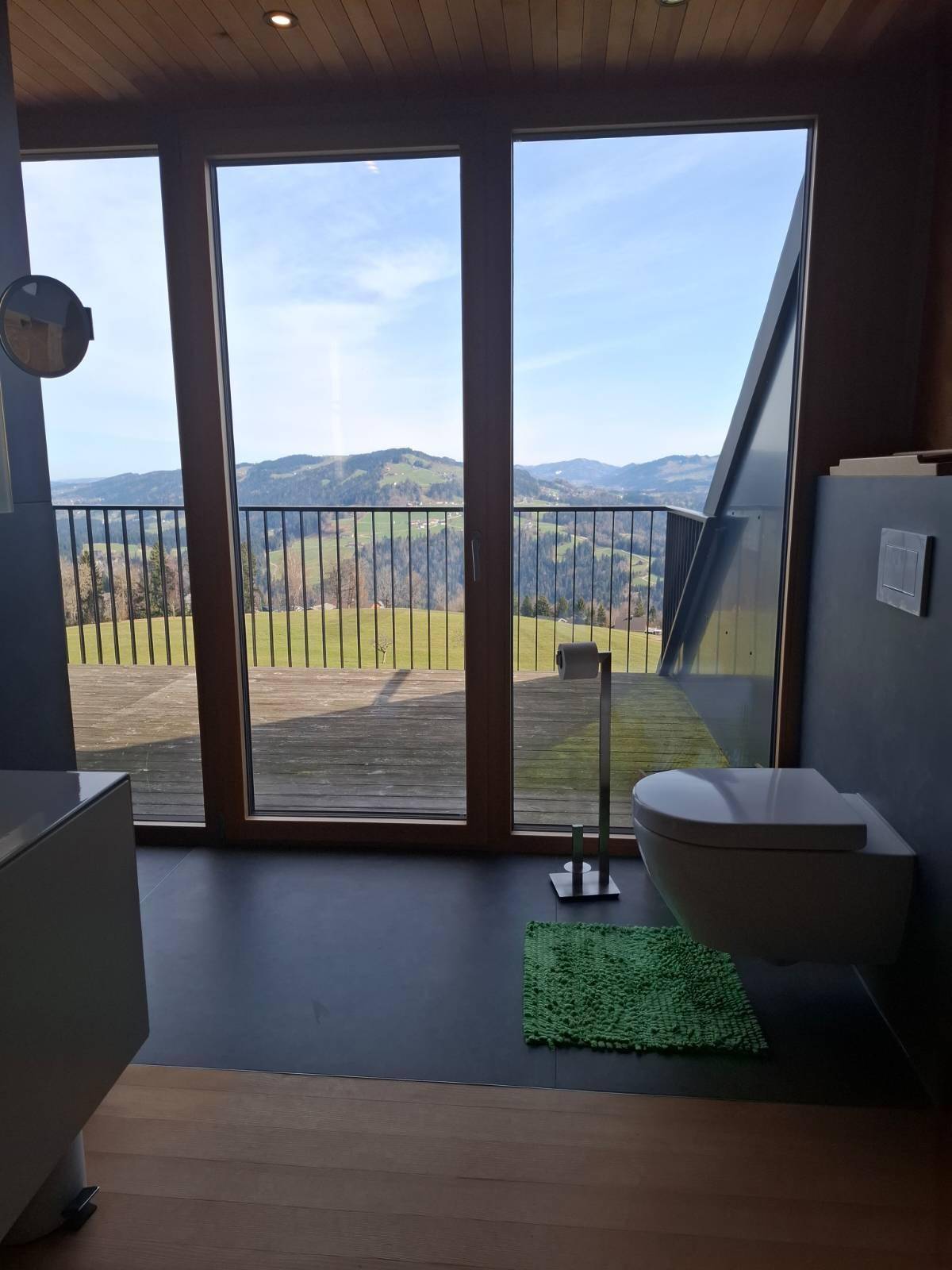 Modernes Badezimmer mit Dusche, WC und großen Fenstern mit weitem Blick auf die Landschaft.