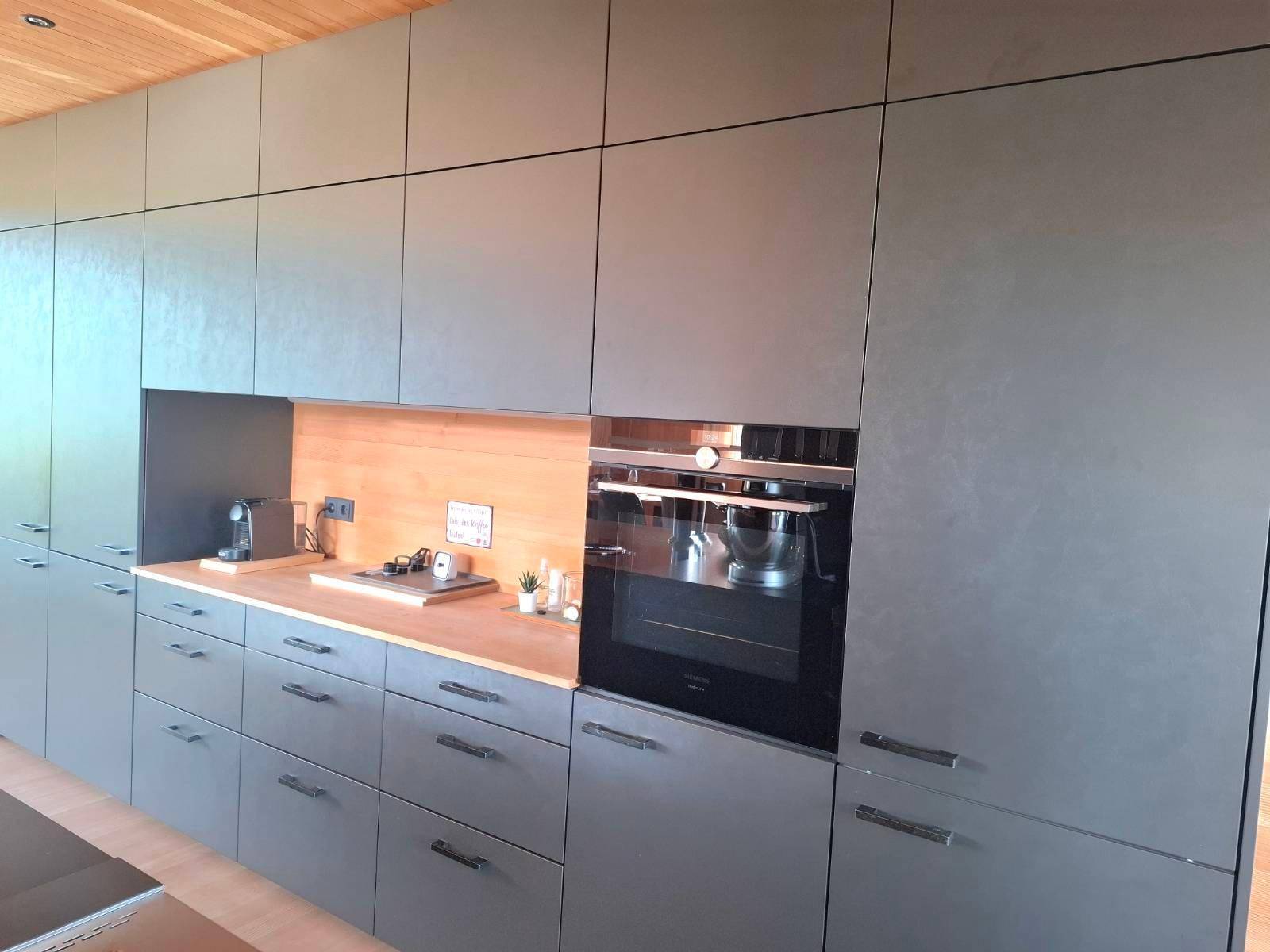 Moderne Einbauküche mit grauen Schränken, integriertem Backofen und Holzarbeitsplatte.