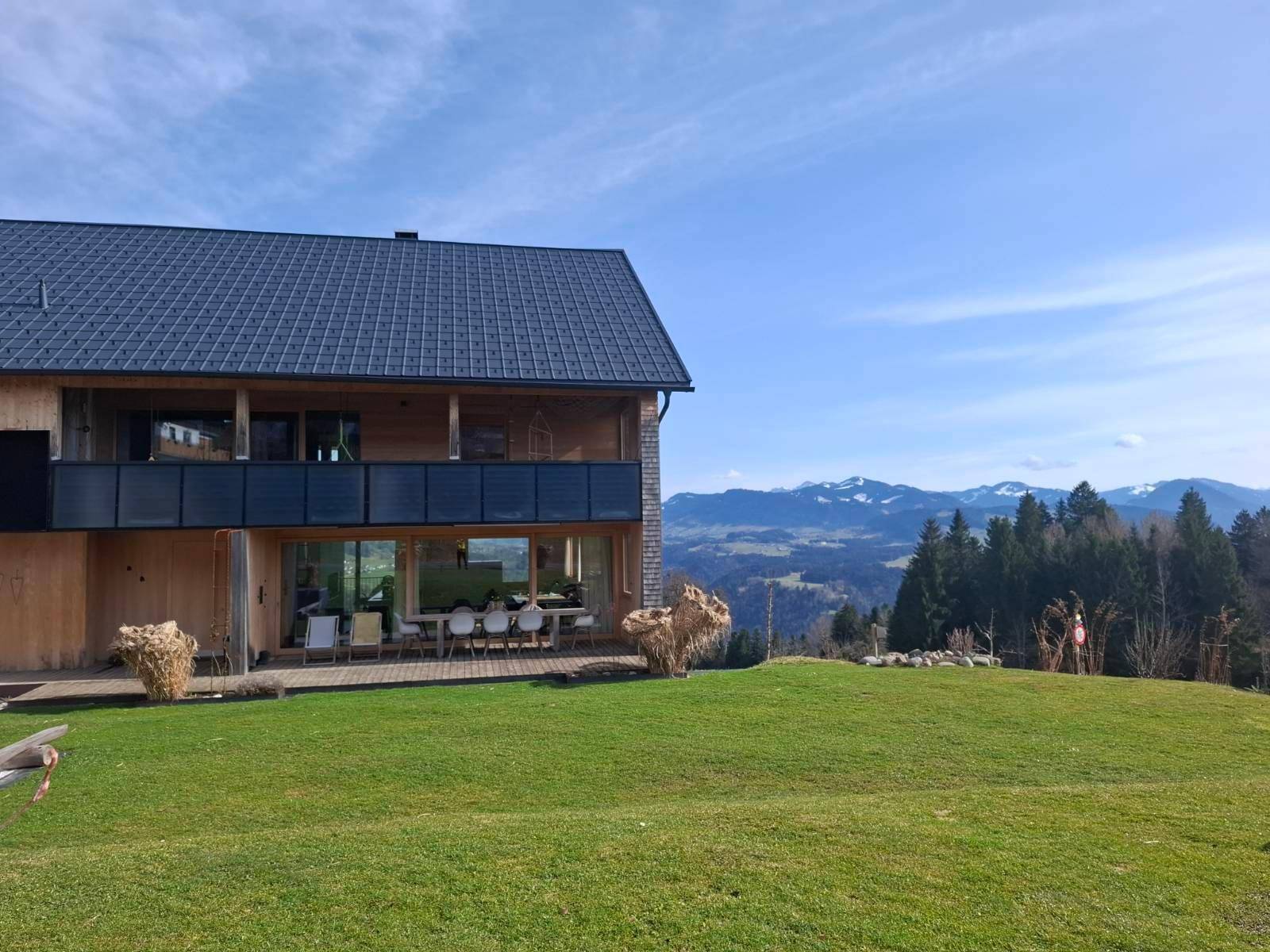 Ansicht des modernen Holzhauses mit großem Garten und Panoramablick auf die umliegende Bergwelt.