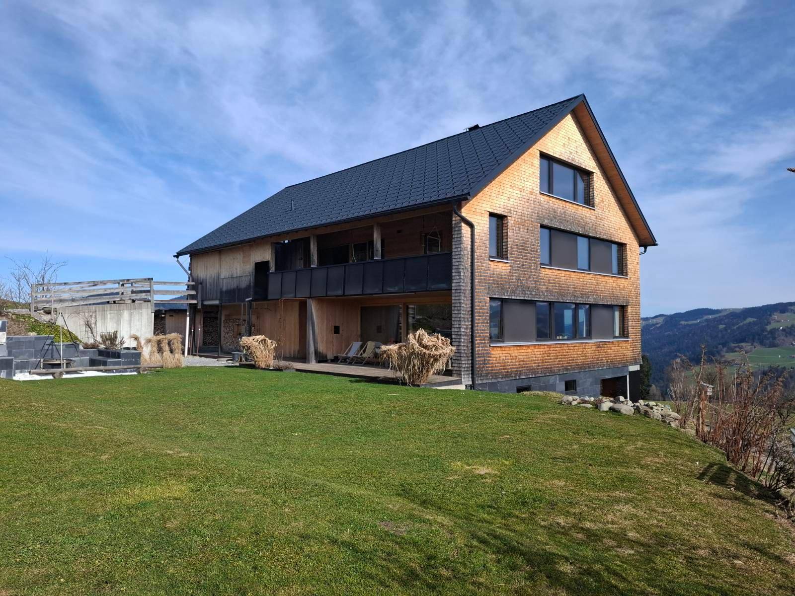 Freistehendes Holzhaus mit Schindelfassade und großem Garten in ländlicher Umgebung mit Bergblick.