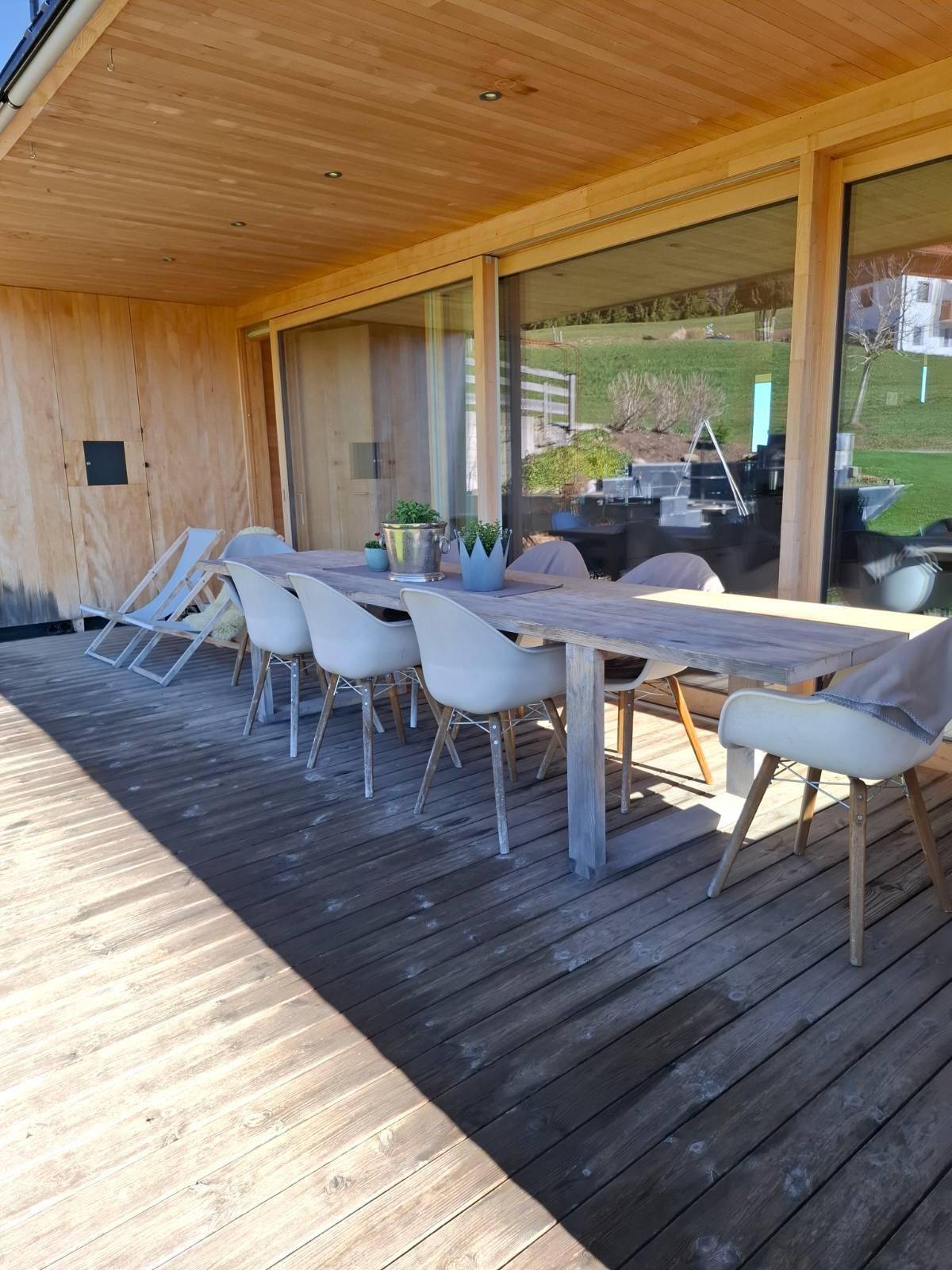 Geräumige Holzterrasse mit langem Esstisch und Stühlen, ideal für Mahlzeiten im Freien mit Aussicht.