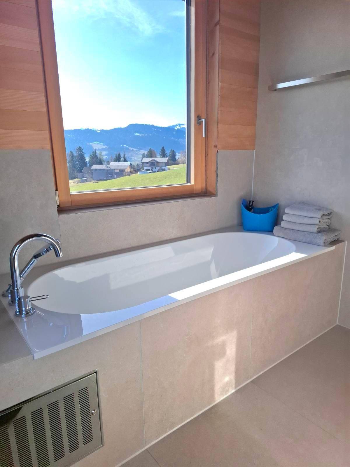 Modernes Badezimmer mit Badewanne, Fenster und Blick auf die grüne Landschaft.