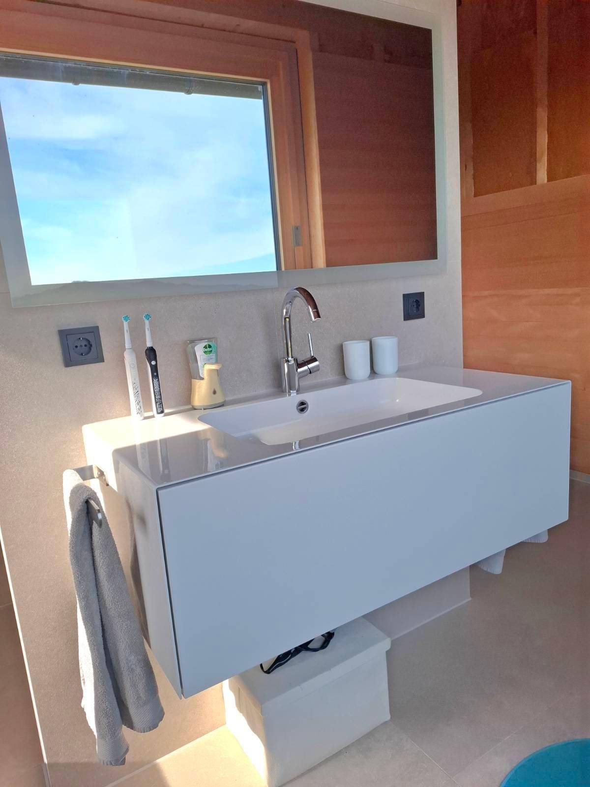 Modernes Badezimmer mit Einzelwaschbecken, beleuchtetem Spiegel und Holzwänden.