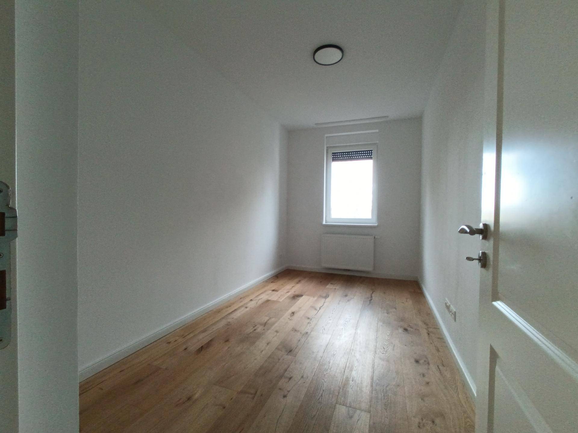 Kleines, helles Zimmer mit Holzboden und Fenster, ausgestattet mit einem Rollladen.