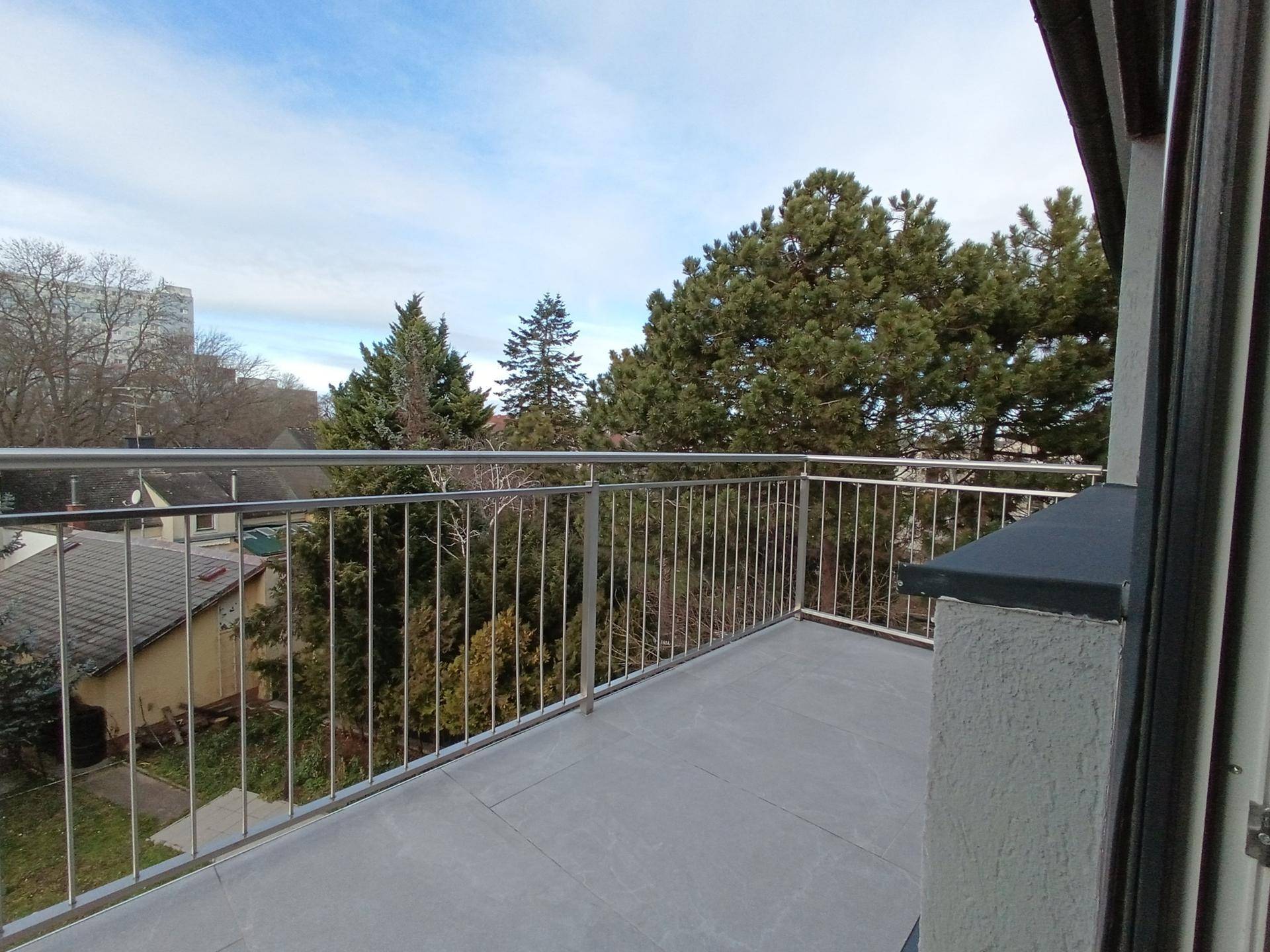 Geräumiger Balkon mit Metallgeländer und Blick auf Bäume und umliegende Häuser.
